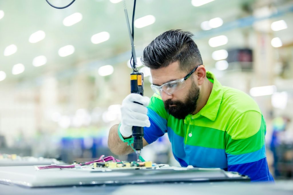 Tecnico con occhiali protettivi al lavoro su un componente elettronico in fabbrica
