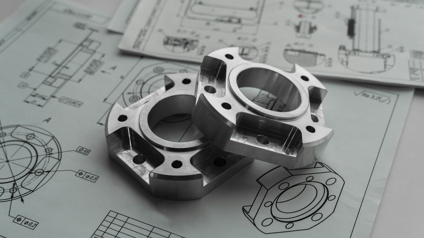 Due componenti metallici appoggiati sui rispettivi disegni tecnici
